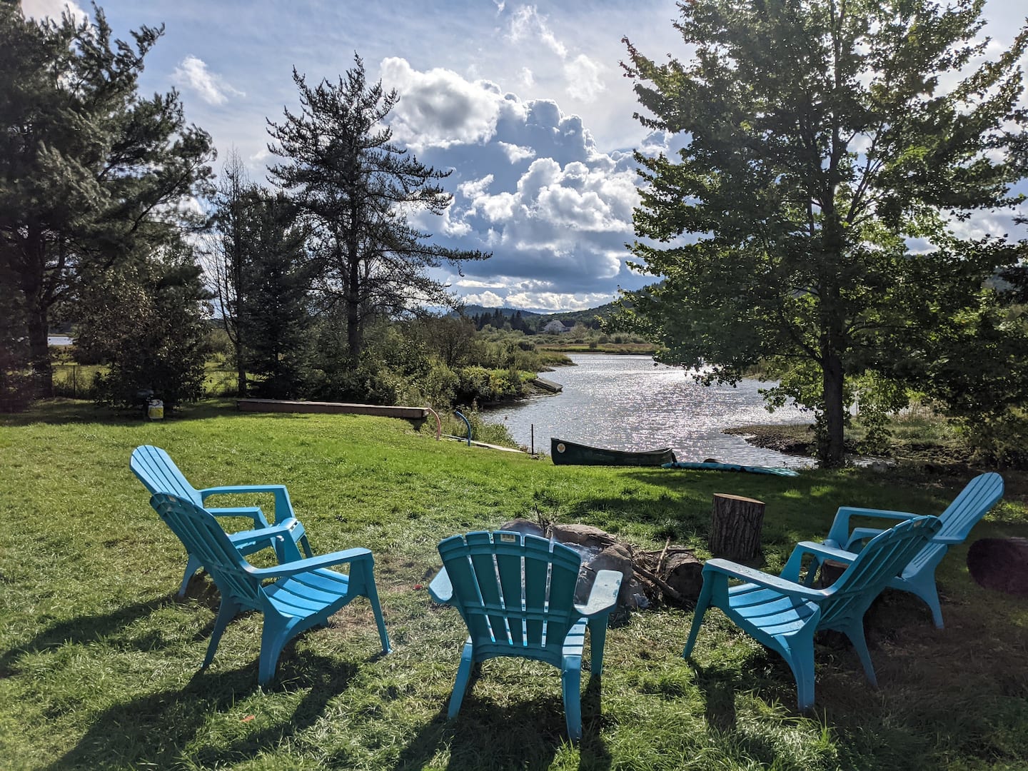 Fire pit with Adirondack chairs beside the water and a canoe